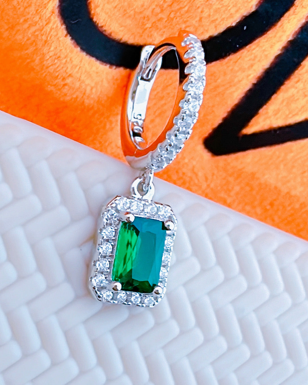 huggie hoop earring with dangling emerald color stone in halo setting.