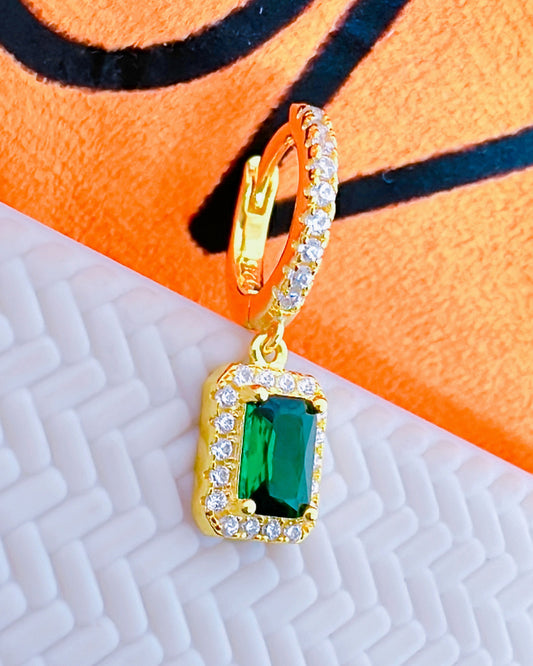 huggie hoop earring with dangling emerald color stone in halo setting.