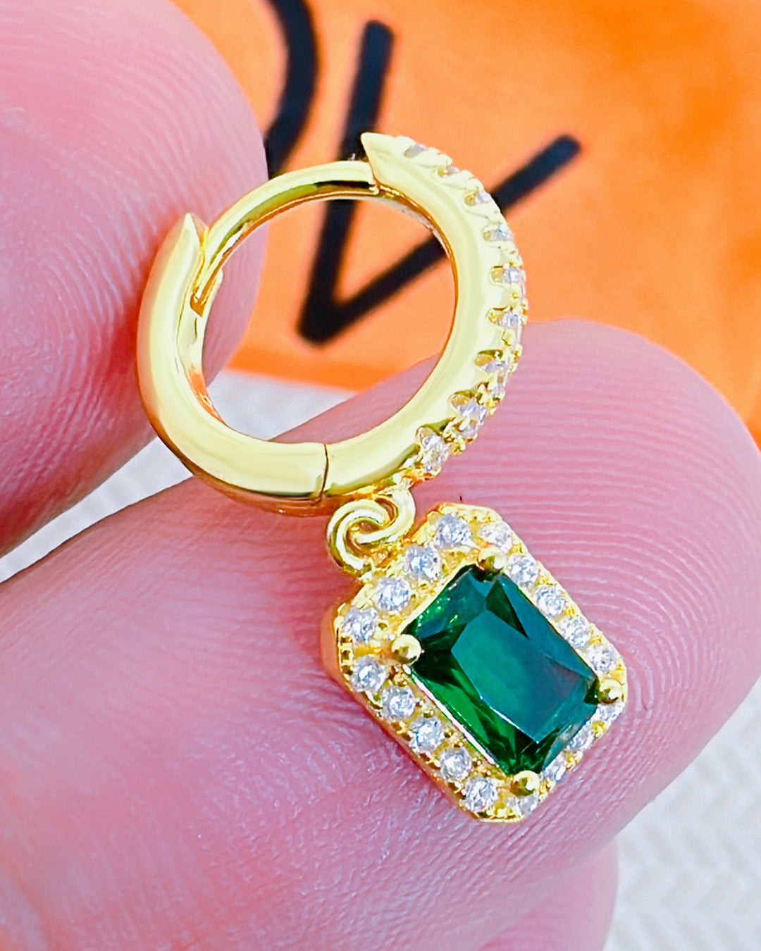 huggie hoop earring with dangling emerald color stone in halo setting.