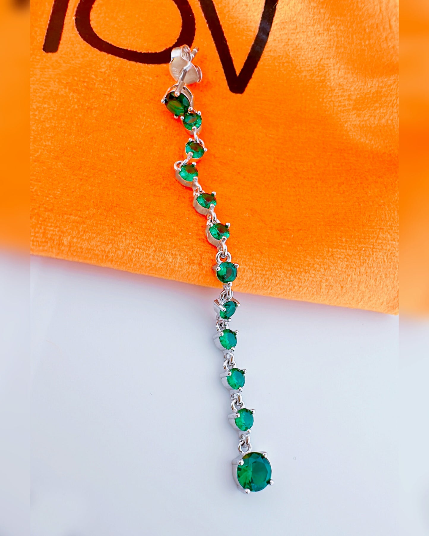 long line of emerald color round stones stud earring.