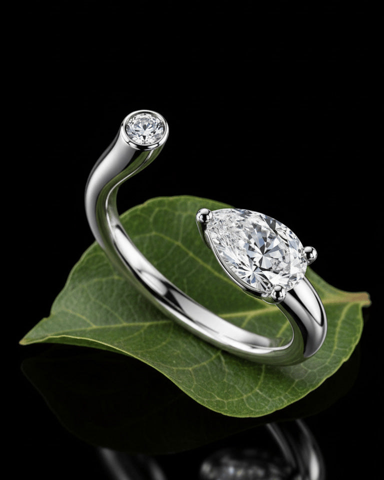 Sterling silver open bypass ring with pear-cut and round bezel-set stones on a green leaf