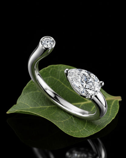 Sterling silver open bypass ring with pear-cut and round bezel-set stones on a green leaf