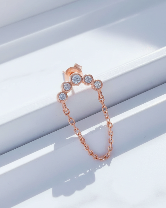 Rosegold curved bar of round CZ in bezel setting with dangling chain.