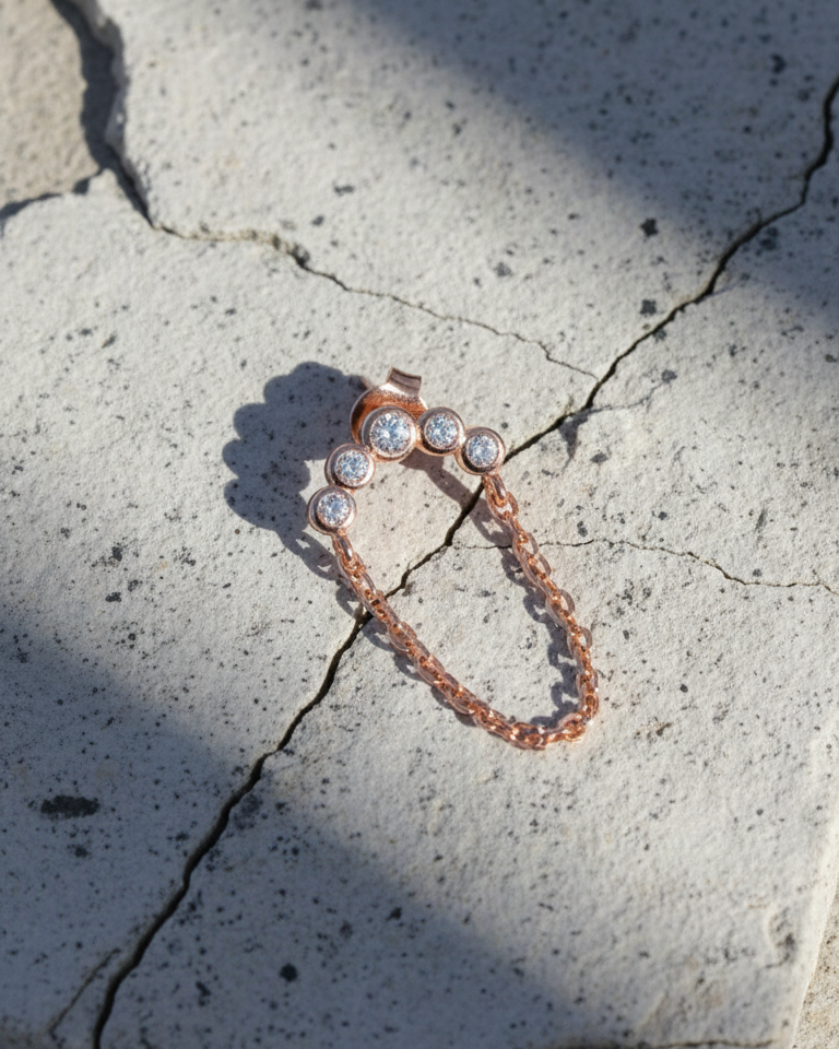 Rosegold curved bar of round CZ in bezel setting with dangling chain.