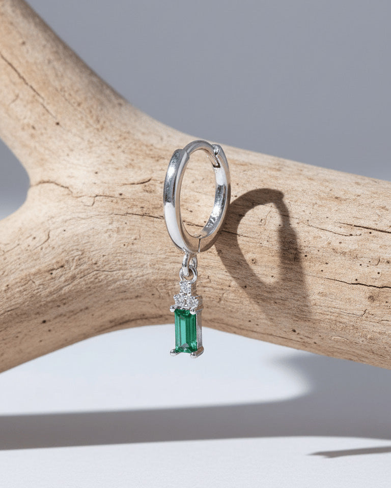 plain silver hoop with dangling emerald cut green stone.