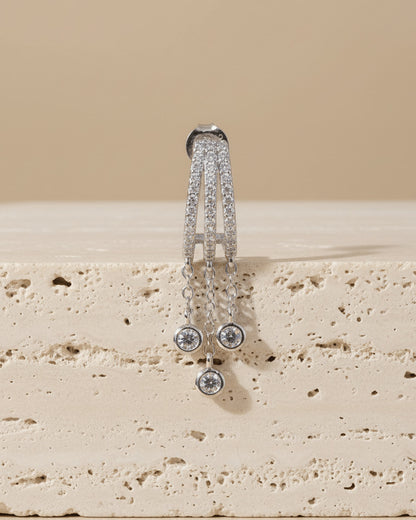 triple half huggie hoop with dangling chains of bezel setting round stones.